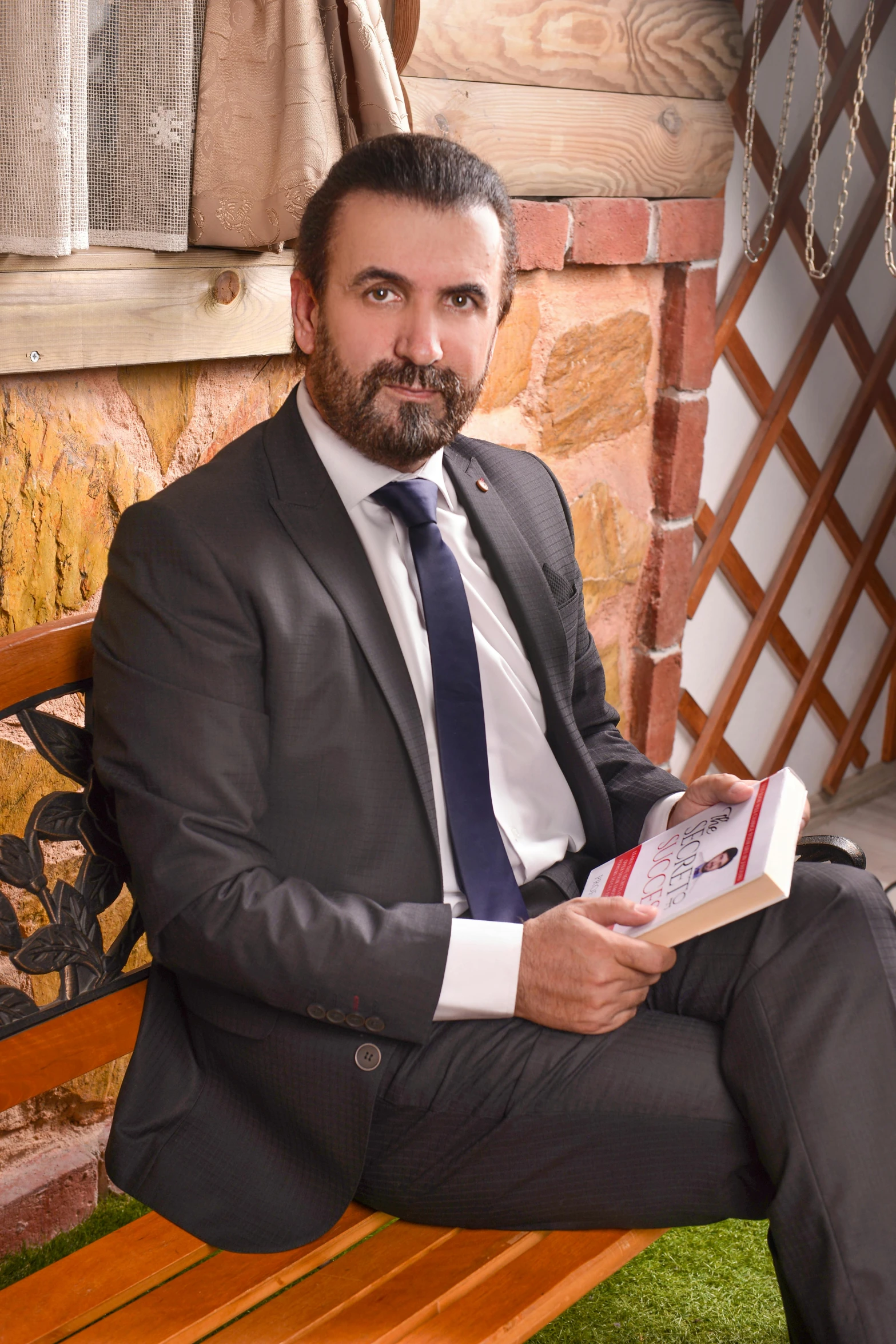 the man in suit sits on a park bench holding an open book