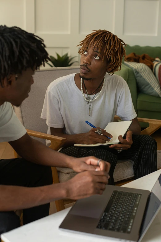 a man sitting next to another mans laptop on a table