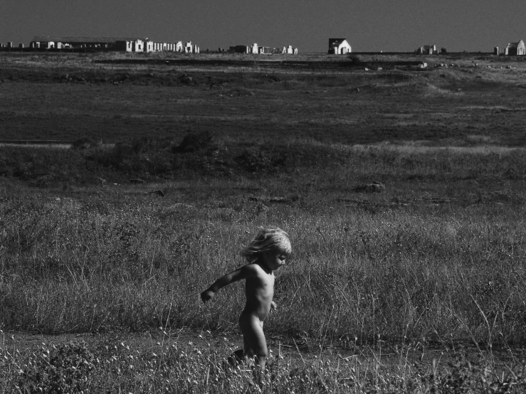 a little baby standing in a field with a bunch of houses