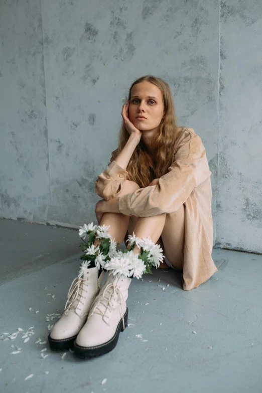 a woman wearing boots sits on the floor with her hands to her face and her head on her hand