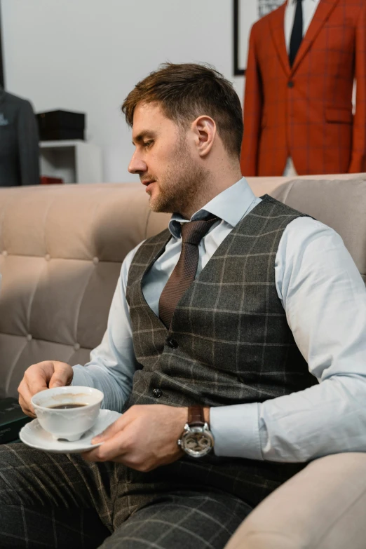 the man sitting in a chair has a cup of coffee and looks at a laptop