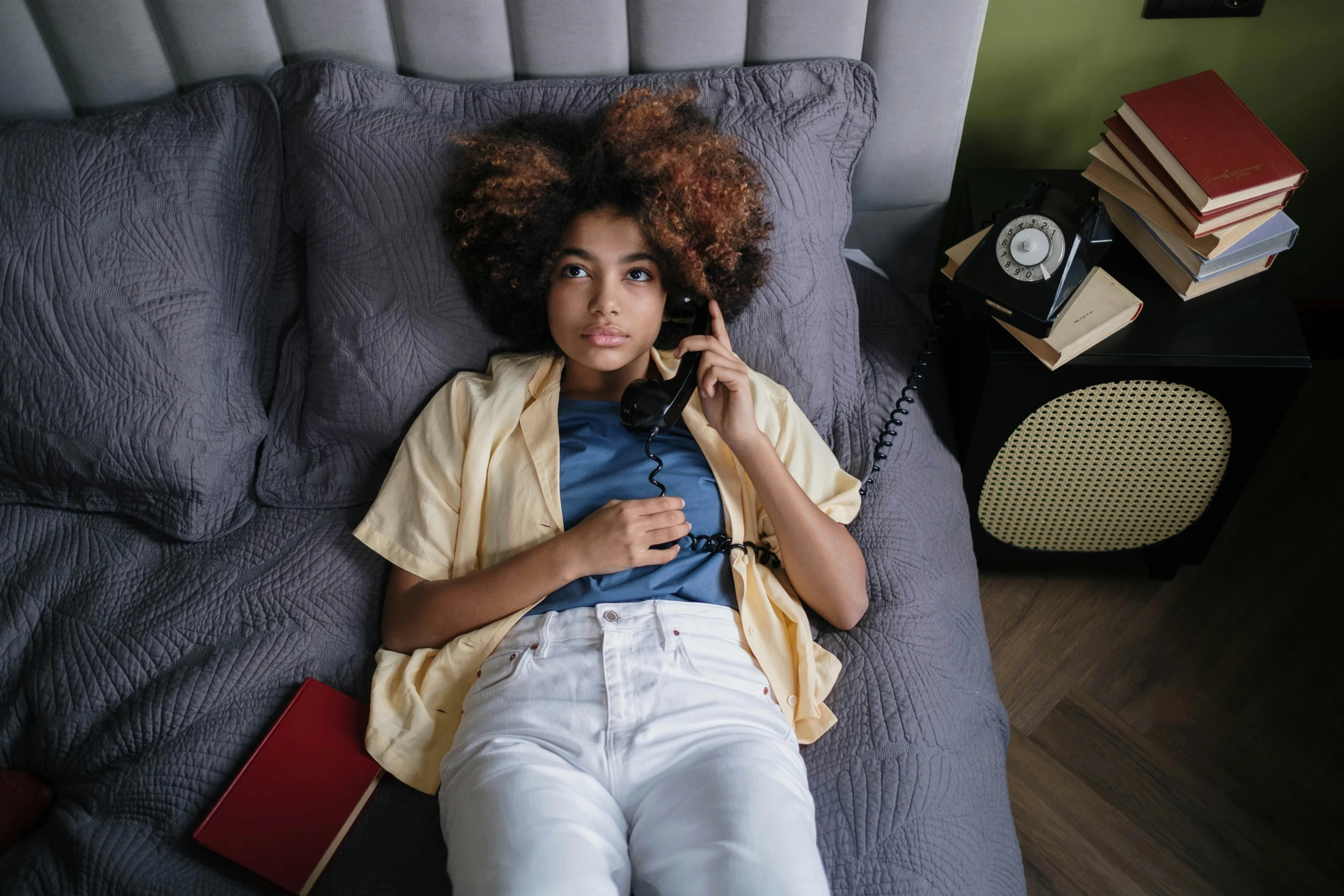 a small girl laying on a grey bed next to a telephone