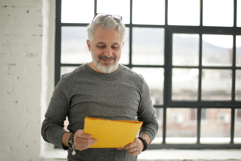 a man in a grey sweater is looking at a yellow folder