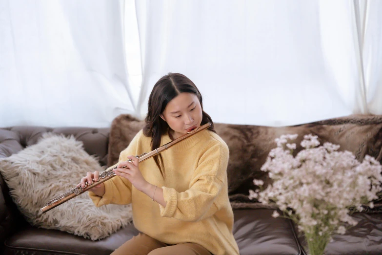 a young woman playing the flute in a room with a brown couch