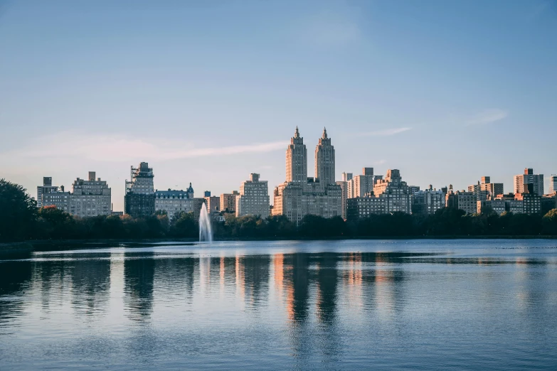 water with a fountain in the foreground, a large city on the far side and tall buildings, in the distance