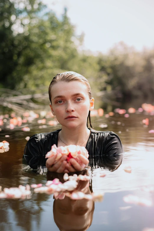 a woman stands in water with flowers floating over her