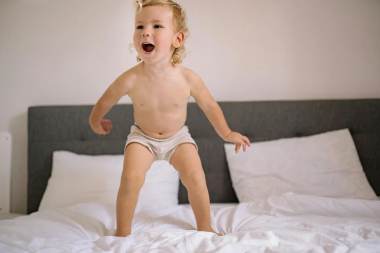  in diaper standing on bed with sheets