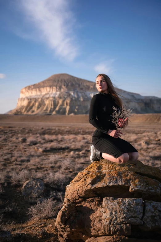 a woman sitting on a rock in the desert with a mountain behind her