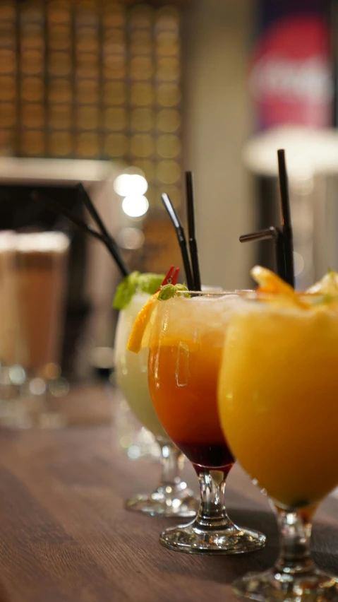 three beverages sit on a bar with black straws in the cups