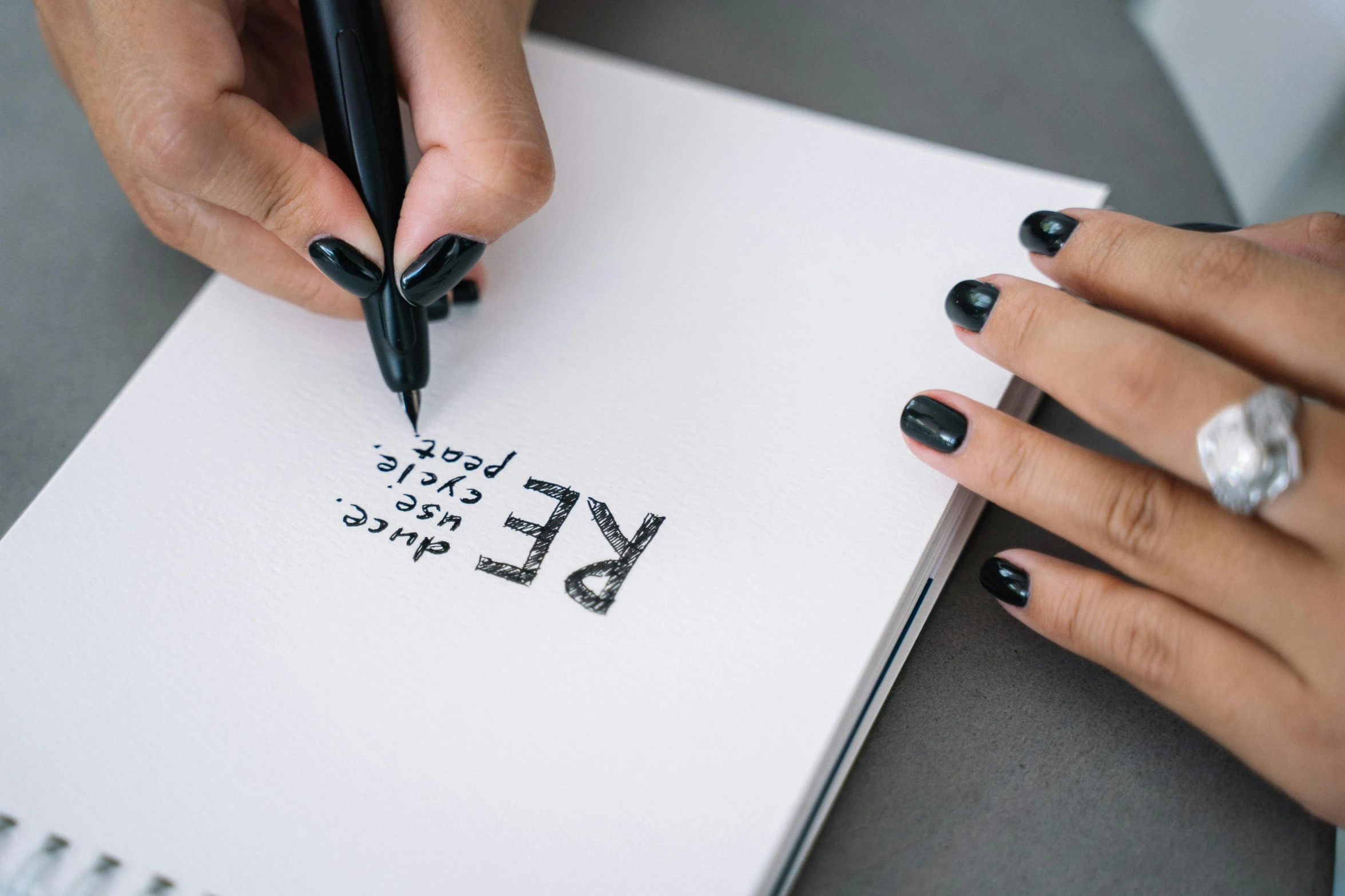 a close up of two hands with black fingernails and black nails writing on a notepad