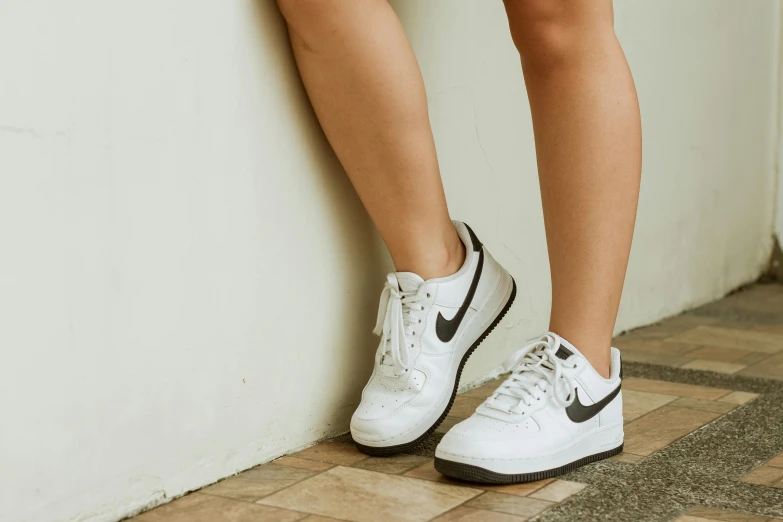 someone in white sneakers is leaning against a wall