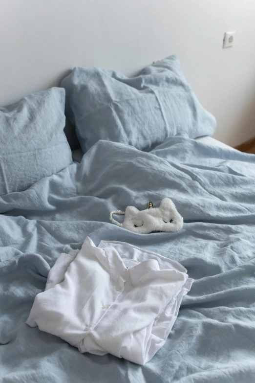 an unmade bed with a light blue cover and a few pillows