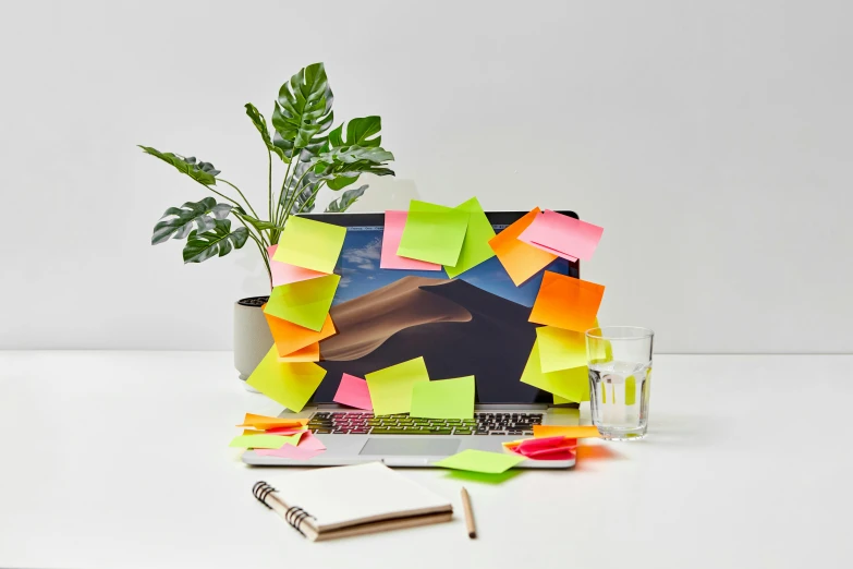 a desk top with an assortment of sticky notes and a plant in it