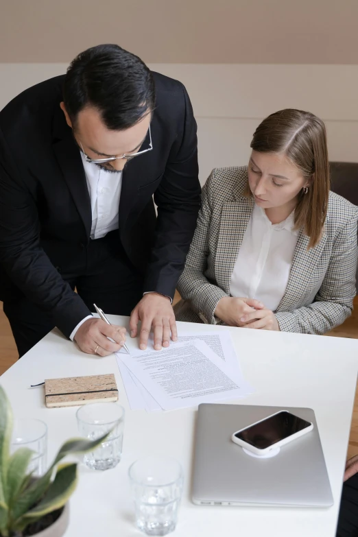 man in suit standing over woman signing a document