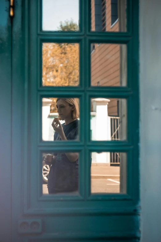 a woman in a blue coat looks out a green door