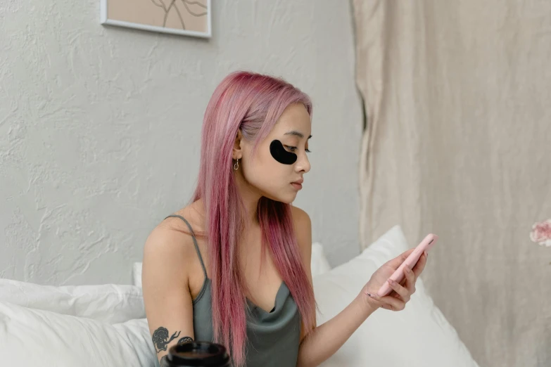 a girl wearing eye glasses sitting on a bed holding up her phone