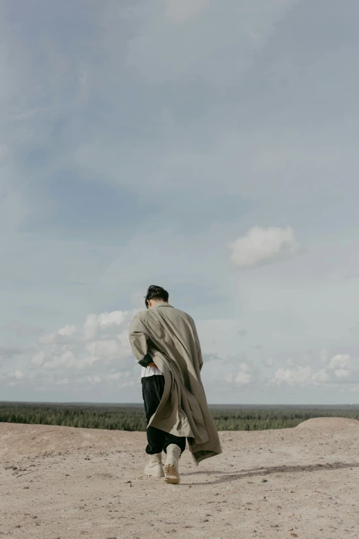 a man in a gray coat walks across an empty beach