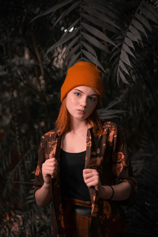 a girl standing with a jacket and hat on in front of plants