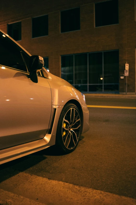 the side view of a silver sport car on a city street at night