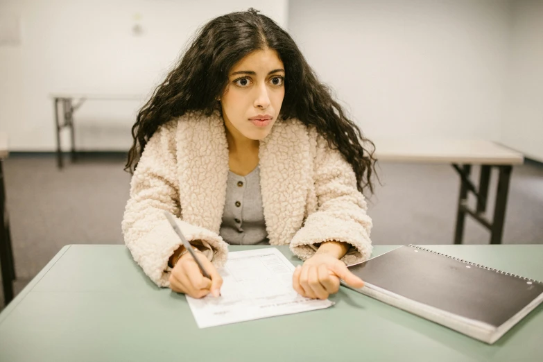 a woman sitting at a table with a notebook and pen