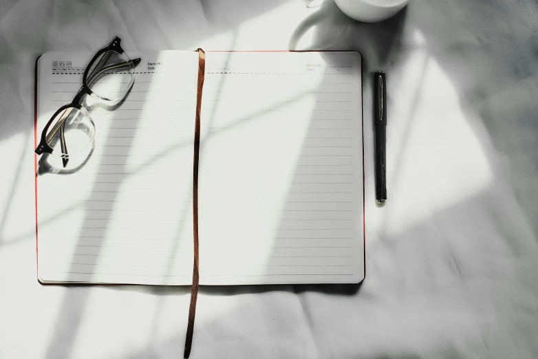 a book with glasses, a pen and a cup of coffee