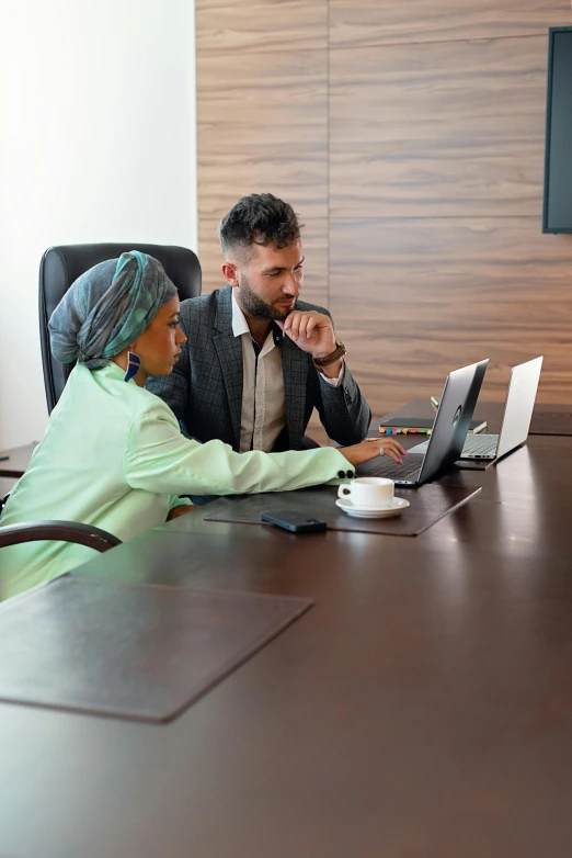 two business people sit at a table looking over a laptop screen