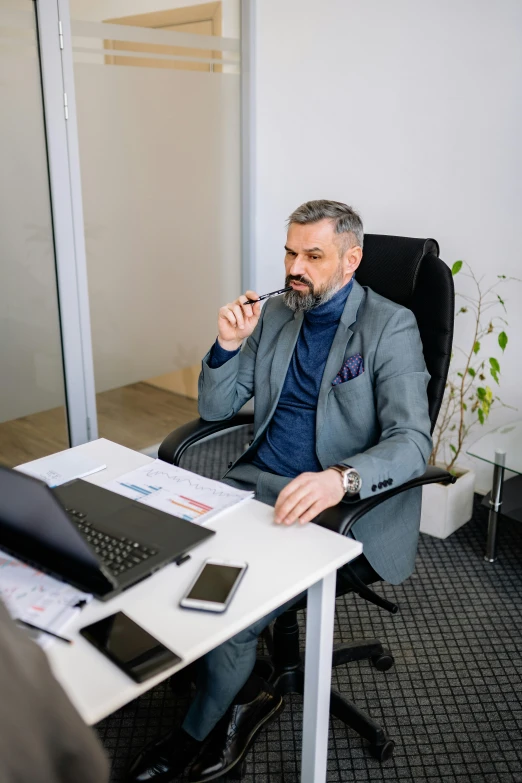 a man sits in a chair at his desk and puts soing to his mouth