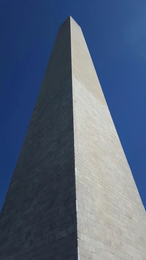 the washington monument with its red clock is silhouetted against a blue sky