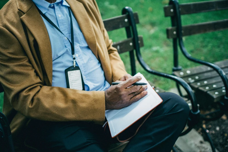 man with writing tablet sits at park bench