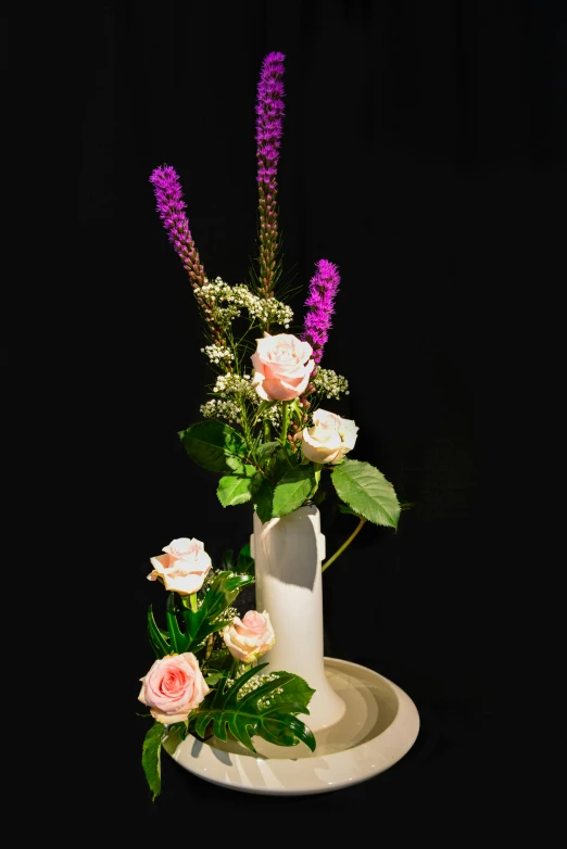 purple flowers in a white vase sitting on a black plate