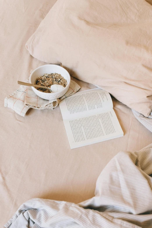 an open book and bowl are on top of a bed