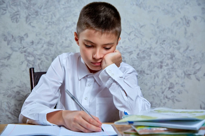 a child sits at a desk in front of books and looks down