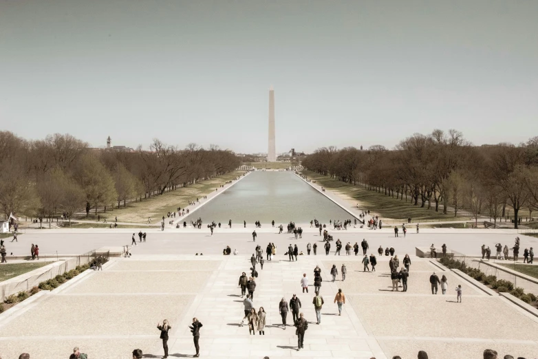 a group of people walking down the sidewalk in front of the washington monument