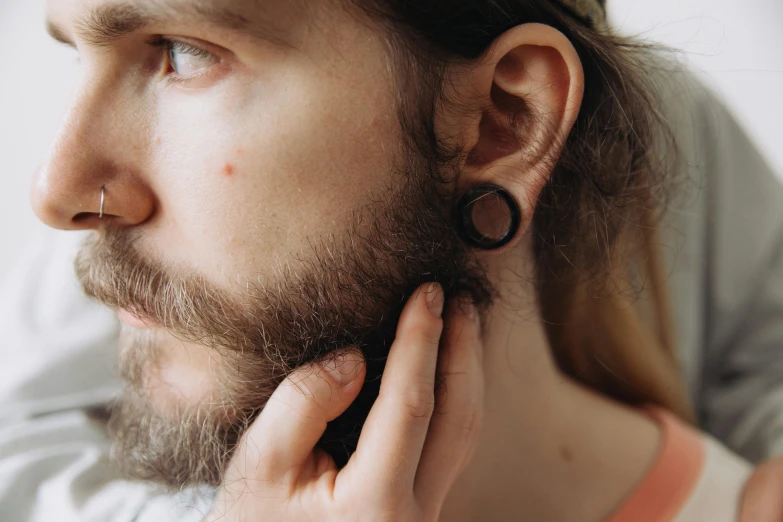 a man putting earrings on his ears while looking away from the camera