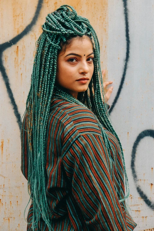 a woman with green dread locks stands next to a graffiti wall