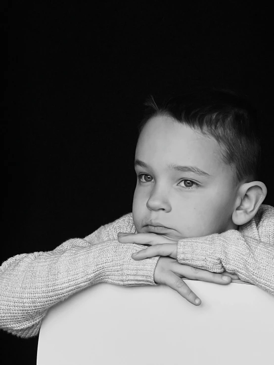 a boy sitting on a white chair looking off in the distance