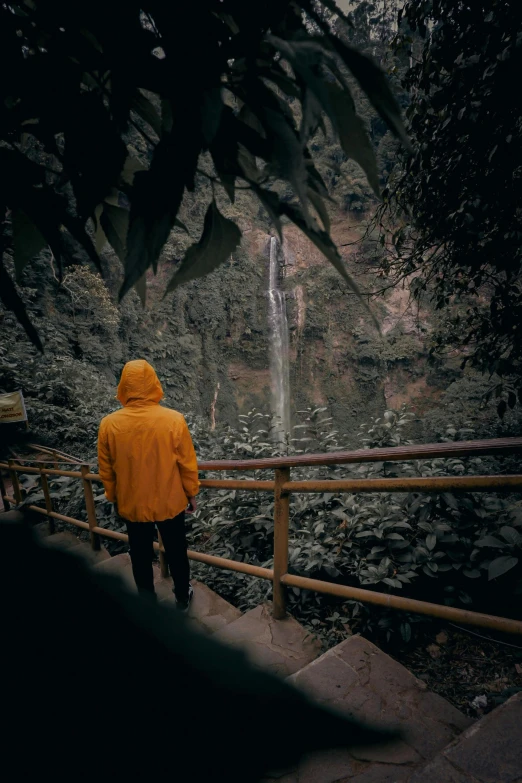 the person in the yellow coat is walking up a steep stair to a waterfall