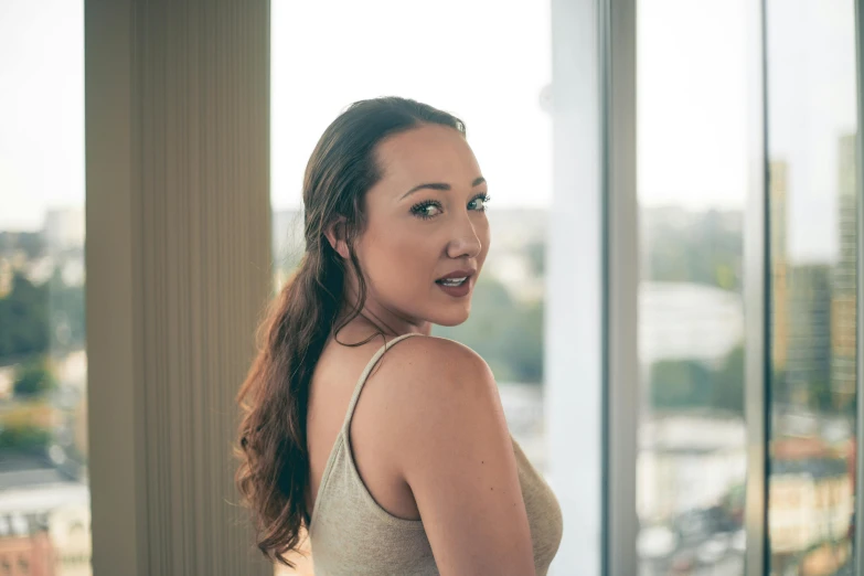 a woman in a white tank top next to windows with a view