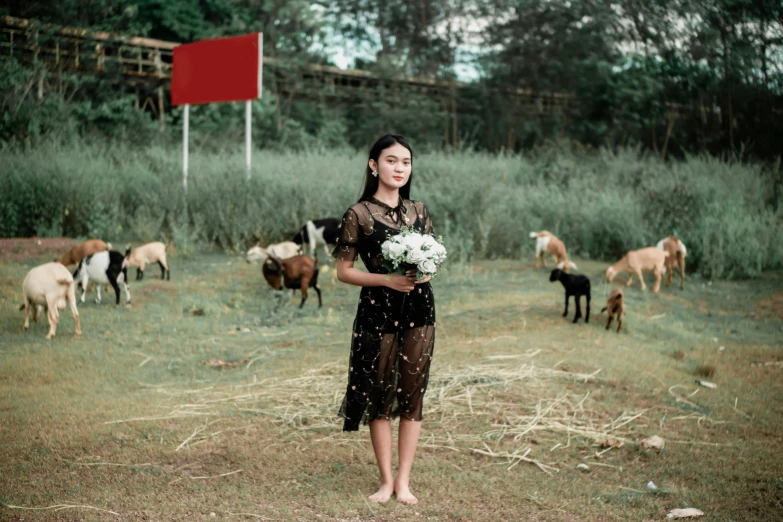 a girl standing with her bouquet in a field with goats