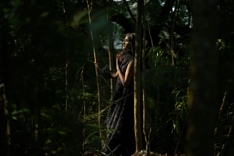 a woman in a dress stands on a platform between tall trees