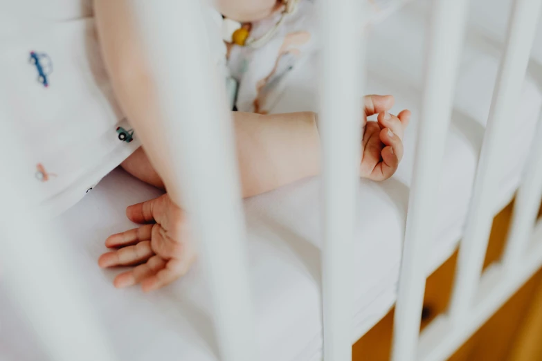 a baby laying in a crib with a hand on a bed