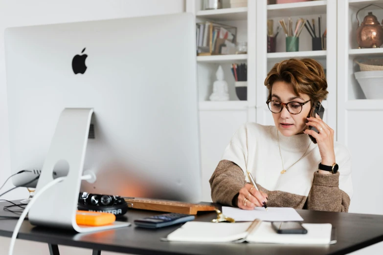 a woman is working on her computer while talking on the phone