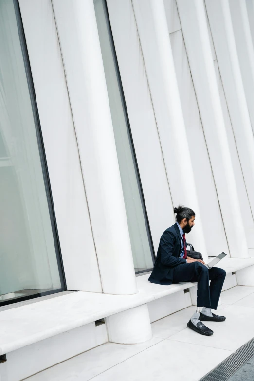 a man in business attire sits on a bench outside of a building