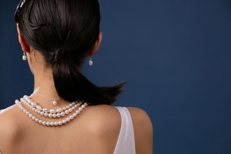 the back view of a woman wearing a dress and pearls necklace