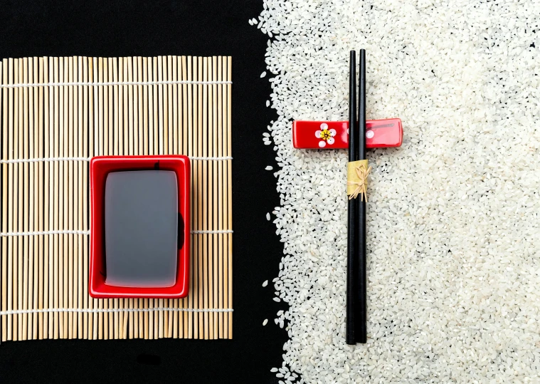 two chopsticks on a mat with a plastic phone next to it