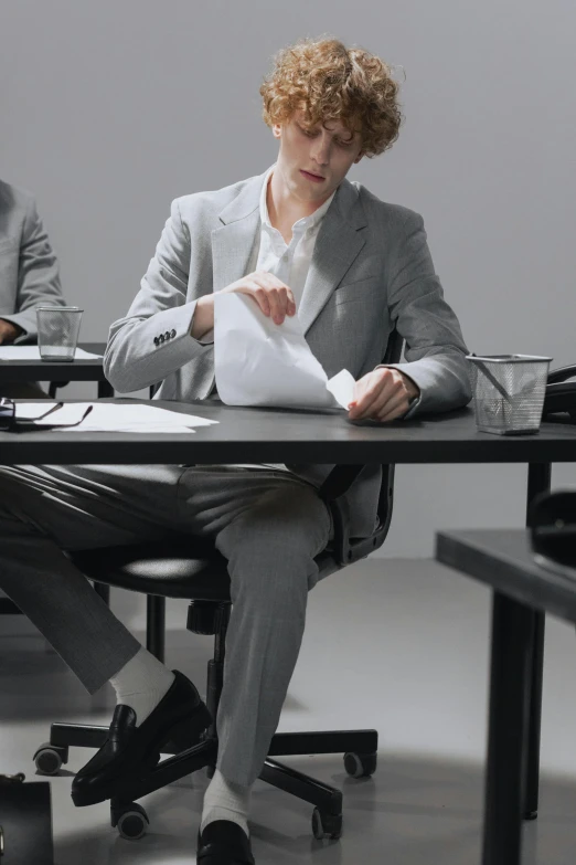 a young man sits at a table and holds papers in his hand