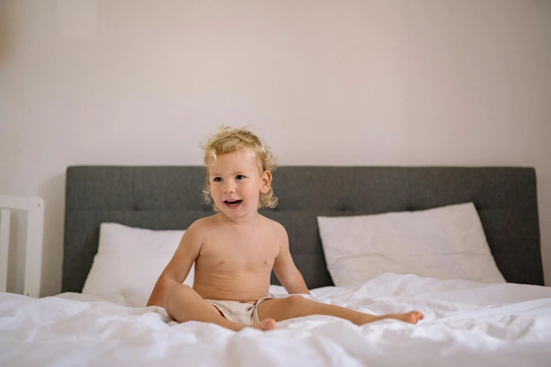 a  sitting on a white bed with his legs crossed