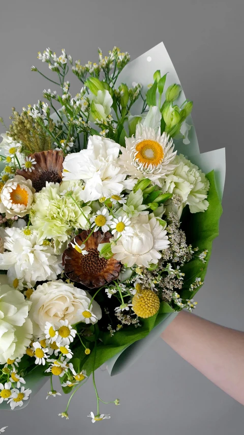 someone holding a large bouquet with white and yellow flowers