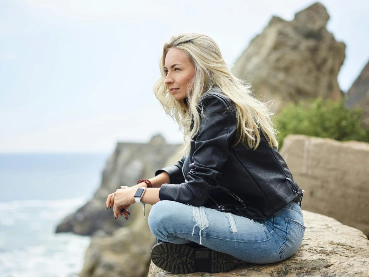 woman sitting on a rock overlooking the ocean in a black jacket