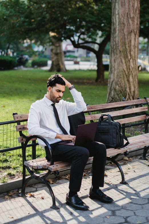 a man in shirt and tie on bench by the tree